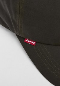 Boné verde escuro com costura visível, apresentando uma etiqueta vermelha da Levi's do lado. O tecido é liso e tem uma forma estruturada.