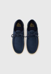 Navy blue suede shoes with a round toe, lace-up design, and beige rubber sole. Features a yellow logo inside. Smooth texture overall.