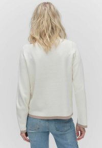 Weißer, strukturierter Pullover mit Rundhalsausschnitt, langen Ärmeln und beigem Saum. Getragen mit blauen Jeans. Rückansicht dargestellt.