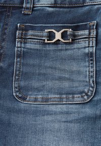 Jeans in denim blu con una tasca posteriore dotata di un accento in metallo argentato e cuciture dorate a contrasto, che accentuano un design di tessuto texturizzato.