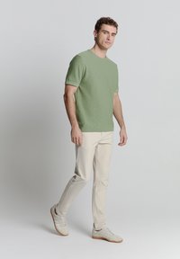 Lichtgroene t-shirt met korte mouwen en een gestructureerde afwerking, gecombineerd met crèmekleurige slim-fit broek en witte sneakers. Eenvoudig ontwerp, geen patronen.