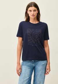 T-shirt à manches courtes bleu marine en coton, avec un design imprimé de pois blancs et le texte "Santorin" à l'avant.