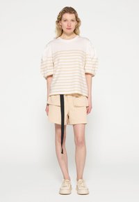 Top a rayas crema con mangas abullonadas, combinado con pantalones cortos de carga beige que cuentan con un cinturón de lazo negro. Footwear casual completa el look.