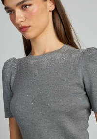 Szary sweter z dzianiny z krótkimi bufiastymi rękawami, ozdobiony akcentami z rhinestones na dekolcie i korpusie, co dodaje tekstury i szczegółów.