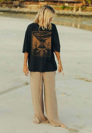 Czarny, oversize'owy t-shirt z grafiką na przodzie oraz beżowe spodnie o szerokich nogawkach. Materiał wydaje się miękki, o luźnym kroju i subtelnej fakturze.