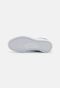 Sola de ténis brancos com grip em borracha texturizada, apresentando um detalhe de meia-sola circular e logótipo em relevo. Superfície lisa com padrão de diamante.