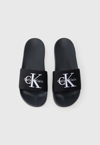 Zwarte slipper sandalen met een stoffen band met het witte "Calvin Klein" logo en de letters "CK." Zachte, platte zool met een gestructureerd oppervlak.