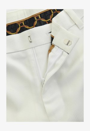 Witte broek met een getextureerd oppervlak, een ritssluiting en een haaksluiting. De binnenzijde van de tailleband toont een patroon van stof.