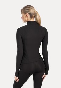 Black fitted long-sleeve top with a high collar, smooth texture, and seam details. Worn with matching black leggings, showcasing a streamlined silhouette.