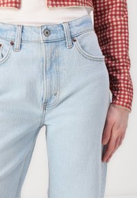 Jeans din denim bleu deschis cu talie înaltă, prezentând o ușoară decolorare, un design cu cinci buzunare și accente de cusătură vizibile.