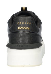 Black sneaker with a textured leather upper, white sole, gold accents, and a looped heel tab. Features CRUYFF branding on the back.