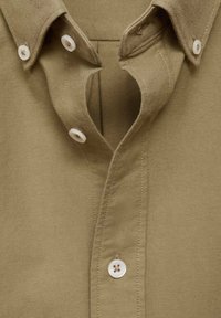 Camicia khaki a bottoni con colletto classico, tessuto semplice e bottoni bianchi. Materiale in cotone testurizzato con finitura pulita.
