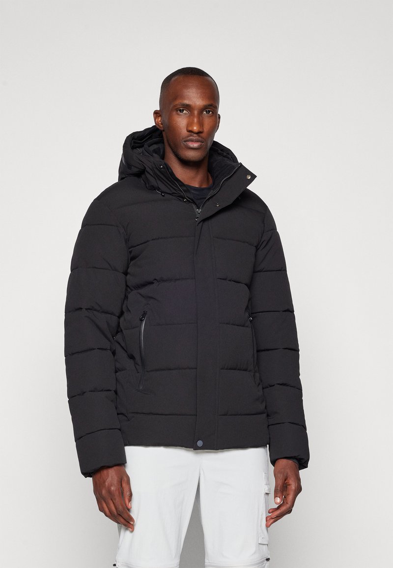 Schwarze Steppjacke mit Kapuze, gestepptem Design, seitlichen Reißverschlusstaschen und einem Druckknopfverschluss vorne. Strukturierter Stoff mit matter Oberfläche.