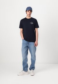 Marineblaues Baumwoll-T-Shirt mit weißer Stickerei, blaue Kappe, hellblaue Jeans und weiße Sneakers. Einfaches Design, lockere Passform.