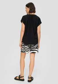 Schwarzes, kurzärmliges Oberteil mit gerafftem Rücken, kombiniert mit weißen und schwarzen Zebra-Print-Shorts und schwarzen Sandalen mit dicker Sohle.