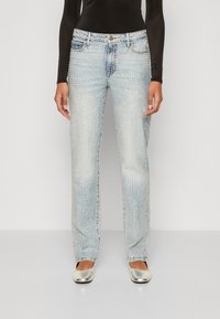 Jeans in denim leggero azzurro con taglio dritto, decorati con borchie scintillanti su tutta la superficie. Abbinati a scarpe piatte argentate.