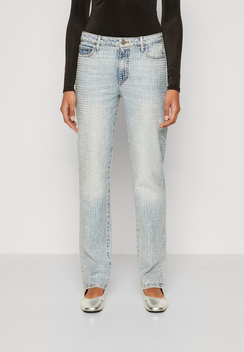 Jeans in denim leggero azzurro con taglio dritto, decorati con borchie scintillanti su tutta la superficie. Abbinati a scarpe piatte argentate.