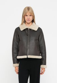 Mørkebrun lærjakke med lys beige pelskrave og mansjetter, med glidelås foran og to sidelommer. Komfortabel og strukturert design.