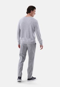 Hellgrauer Strickpullover mit Rundhalsausschnitt, kombiniert mit hellgrauen karierten Hosen und dunklen Sneakern, von hinten betrachtet.