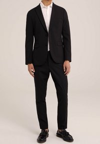 Svart skräddarsydd kostym med enkelknäppt blazer, snibbade slag och två knappar. Matchad med slim fit svarta byxor och svarta skor.