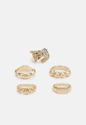 Conjunto de cinco anéis de ouro: um com um design de gato e pedra clara, os outros apresentam detalhes lisos, texturizados e com contas, com formas e designs variados.