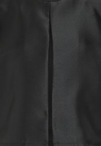 Svart plagg gjort av ett slätt tyg med en subtil glans. Har en bakre slits för rörelse och en strömlinjeformad design utan synlig hårdvara.