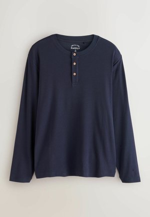 Mornarica dugačka majica s dugim rukavima, okruglim izrezom, plaketom s tri gumba, rebrastom teksturom i ravnim rubom. Napravljena od prozračnog materijala.