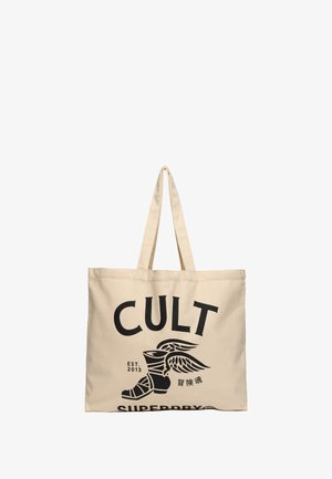 Beżowa torba płócienna z wyraźnym czarnym napisem "CULT" oraz grafiką skrzydlatej buty. Solidny materiał i długie rączki do łatwego noszenia.