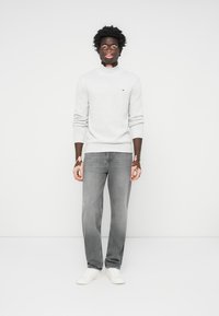 Lys gråstrikket genser med rund hals, kombinert med medium grå denimjeans og hvite sneakers. Har en liten logo på genseren.