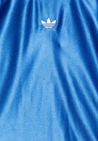 Niebieska koszulka sportowa z teksturowanej tkaniny, z białym logo Adidas i trzema paskami, umieszczonym centralnie nad strefą klatki piersiowej.