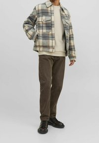 Rutete uldjakke i grå, creme og brun med to brystlommer. Båret over en beige sweater og olivengrønne bukser, suppleret med sorte støvler.