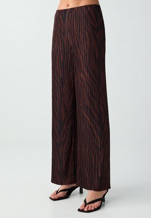 Pantalon à jambe large avec un motif zigzag géométrique noir et marron, porté avec des sandales noires à talons, raccourci sous la taille.