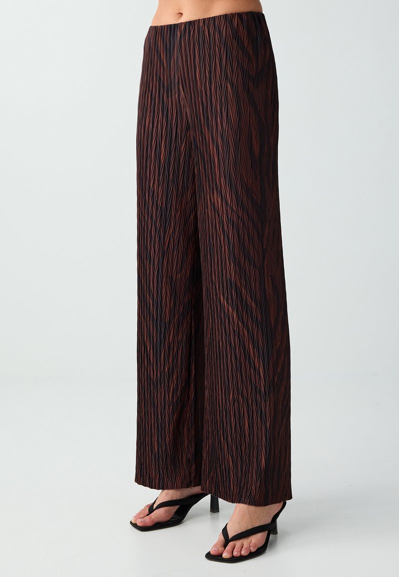 Pantalon à jambe large avec un motif zigzag géométrique noir et marron, porté avec des sandales noires à talons, raccourci sous la taille.