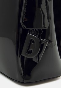 Svart lackläderväska med en slät, glansig yta. Har en distinkt logotags i geometrisk design som tillför visuell intresse.