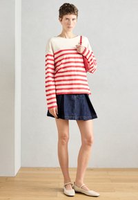 Sarkana un balta svītrainā krekls ar garām piedurknēm, apvienots ar tumši džinsu A formas svārkiem. Modelis valkā gaiši beigu dzīvokļa apavus. Minimālistisks dizains.