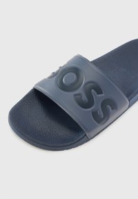 Mørkeblå glidesandal med en teksturert fotseng, en tykk stropp med hevede bokstaver og en glatt gummioverflate.