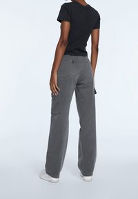 Grijze cargo broek met wijde benen, zijzakken, contrasterende stiksels en een iets vervaagde afwerking. Gecombineerd met een aansluitend zwart t-shirt.