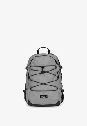 Sac à dos gris avec une finition texturée, présentant des accents noirs, des cordons élastiques à l'avant, des poches latérales en mesh doubles et une poignée de transport supérieure.