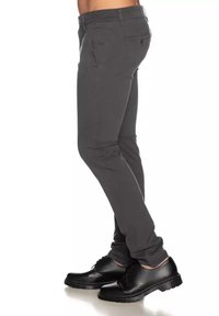 Pantaloni grigi attillati con tasche laterali, passanti per cintura e una texture liscia; indossati con scarpe nere stringate con suola spessa.