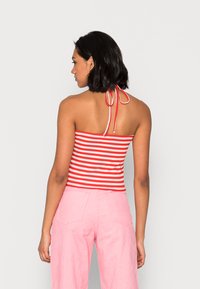 Top sem mangas riscado em vermelho e branco com um laço nas costas, combinado com calças largas de tom rosa claro. Tecido suave com textura canelada.