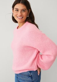 Maglione rosa chiaro realizzato in materiale morbido e strutturato, con scollo rotondo e vestibilità rilassata, abbinato a jeans blu.