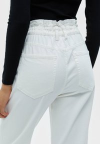 Weiße, hochgeschnittene Jeans mit einem gerafften, elastischen Bund, die über zwei Gesäßtaschen und einen glatten, strukturierten Stoff verfügt.