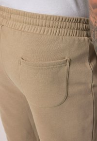 Beige sweatpants with an elastic waistband, featuring a back pocket, made from soft fabric with a smooth texture.