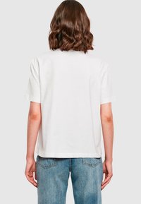 Weißes T-Shirt aus Baumwolle mit kurzen Ärmeln und lässigem Schnitt, mit einem schlichten Rückendesign und geradem Saum, kombiniert mit hellen Jeans.