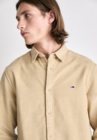 Camicia in corduroy beige con chiusura a bottoni, dotata di un piccolo logo ricamato sul petto e colletto classico.