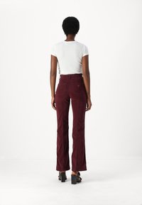 Pantaloni a palazzo in corduroy bordeaux con vita alta e due tasche posteriori, abbinati a una t-shirt aderente bianca a righe. Sandali neri con tacco.