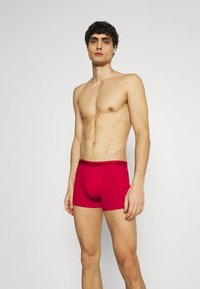 Punaiset boxerit mustalla vyötärönauhala, jossa on "TOMMY HILFIGER" -logo. Valmistettu pehmeästä kankaasta, istuva malli sileällä pinnalla.