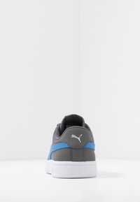 Šedé a modré tenisky s hladkým syntetickým svrškem, bílou podrážkou a texturovanými detaily, s logem na patě.