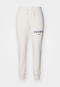 Kermanväriset collegehousut, joissa on joustava vyötärönauha, nyöritys, kapenevat lahkeet ja vasemmassa reidessä painettu "NIKE"-logo tummansinisenä.