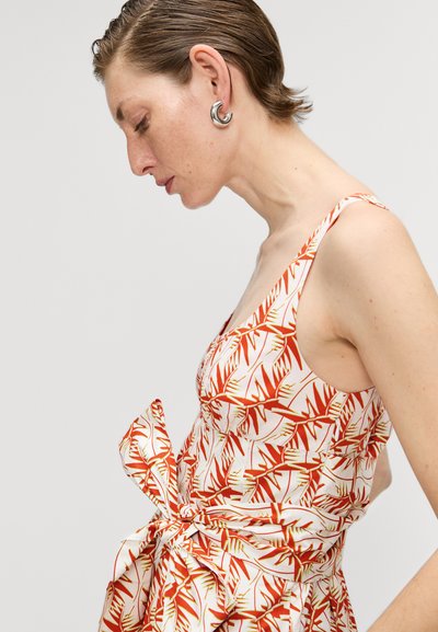 Weißes Kleid mit einem roten und grünen Blättermuster, mit einem taillierten Oberteil und einer gebundenen Schleife an der Taille, aus leichtem Stoff.